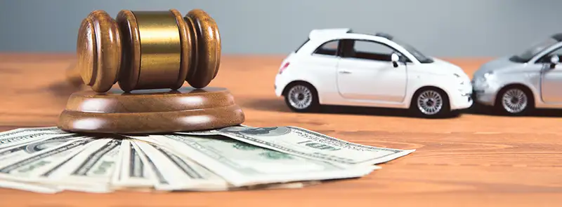 Gavel on top of a stack of cash next to two toy cars