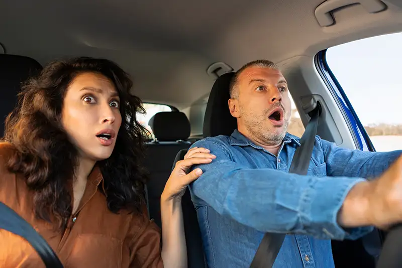 Man driving with a female passenger, both with faces in shock