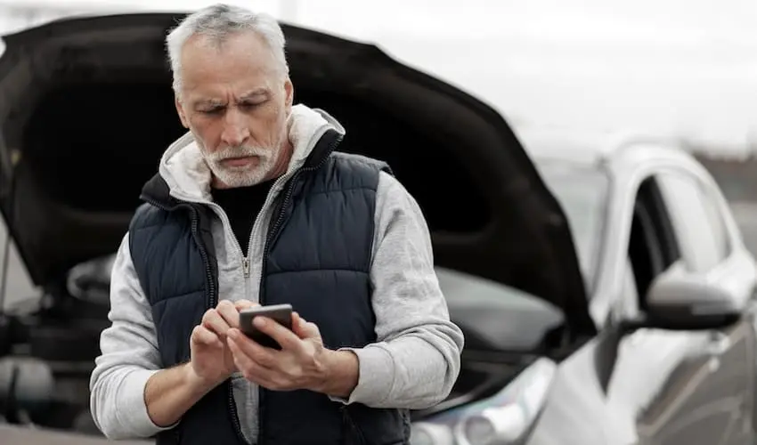 The motor vehicle accidents victim is using a smartphone to contact the insurance company at the collision scene.