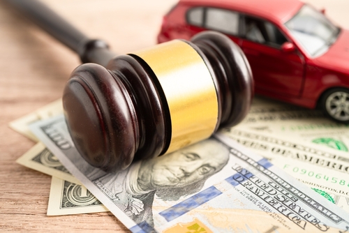 Gavel on top of dollar bills and a car representing a legal case for a victim who lost wages after a car accident.