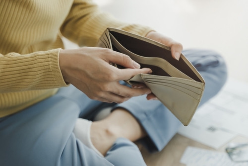 Woman sitting on the floor with bills on the floor opening her empty wallet illustrating lost wages after a car accident.