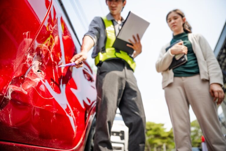 An insurance adjuster is documenting a damaged red vehicle for a car accident claim investigation and assessment in Atlanta.