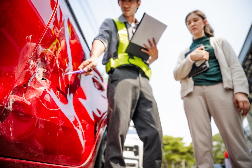 An insurance adjuster is documenting a damaged red vehicle for a car accident claim investigation and assessment in Atlanta.