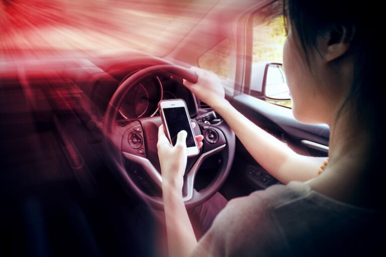 A woman is looking down at her smartphone while gripping the steering wheel while a dramatic red blur effect illustrates the split-second danger of a texting while driving accident in Atlanta.