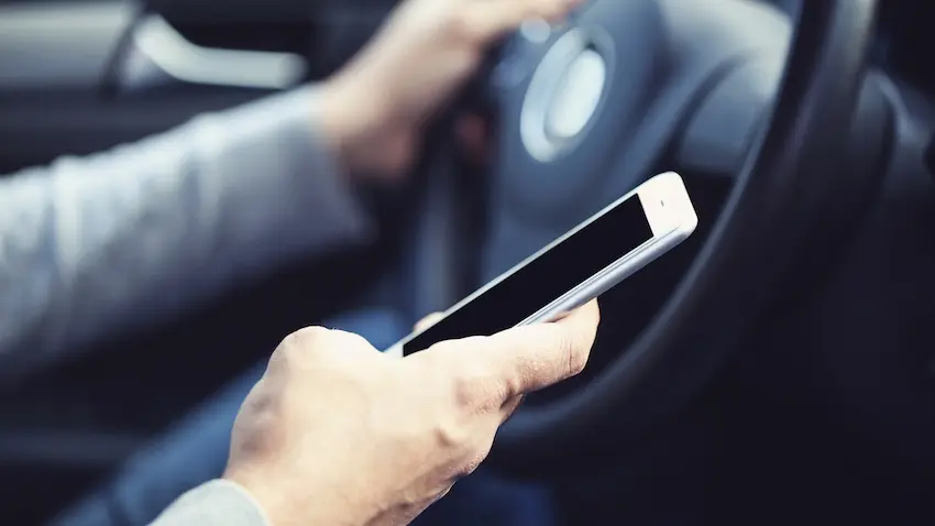 A close-up of a driver's hand holding a smartphone in front of the steering wheel capturing the distracted behavior that commonly leads to a texting while driving accident in Atlanta.