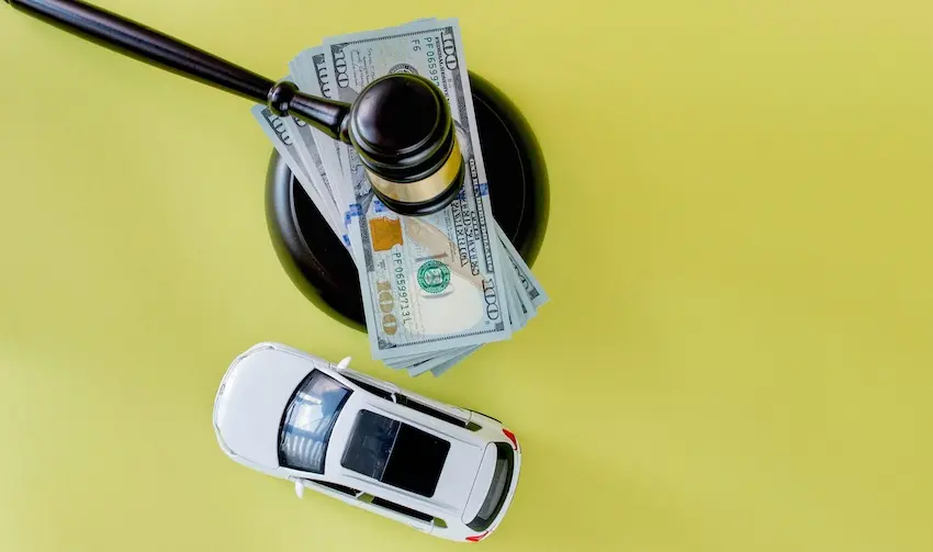 A judge's gavel is resting on a stack of hundred-dollar bills beside a toy car on a yellow background representing the legal and financial consequences that follow a texting while driving accident and the helpful assistance that someone could use from Hodgins & Kiber LLC.