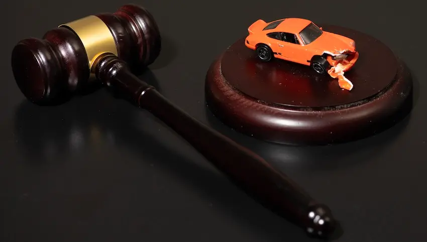 A damaged orange toy car sits atop a judge's gavel sound block beside a dark wooden mallet on a black surface symbolizing the legal proceedings that follow when a victim pursues justice after a hit-and-run accident with help from Hodgins & Kiber LLC.