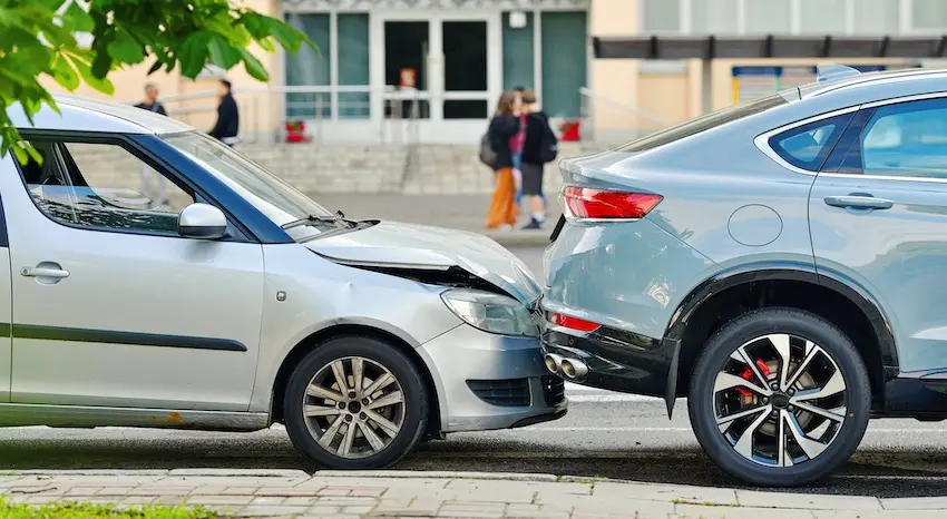 A compact silver sedan has its front end crumpled into the rear bumper of a larger silver SUV on a city street with pedestrians visible in the background showing the direct point of impact in a classic scenario where one driver is rear-ended at low speed and could use legal representation from Hodgins & Kiber LLC.