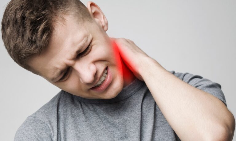 A young man in a gray t-shirt grimaces and clutches the back of his neck with a red pain indicator highlighting the injury site visually representing the whiplash and cervical strain that are the most common injuries suffered when a driver is rear-ended in Metro Atlanta.