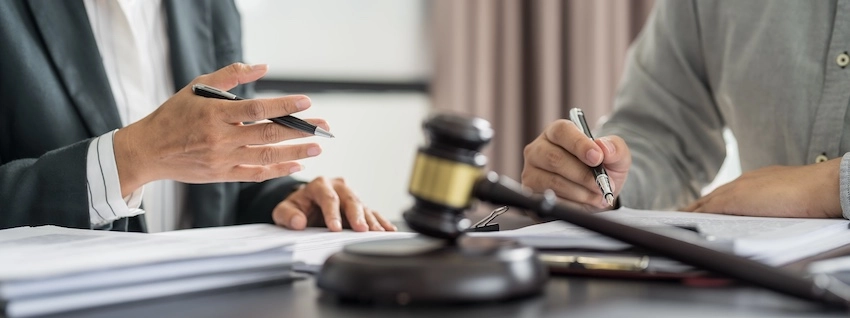 An attorney from Hodgins & Kiber LLC gestures firmly with a pen toward a client across a desk bearing a judge's gavel and stacked legal documents- representing the tense negotiation that often occurs when an injury victim disputes the findings of an insurance adjuster with the help of legal counsel in Metro Atlanta.