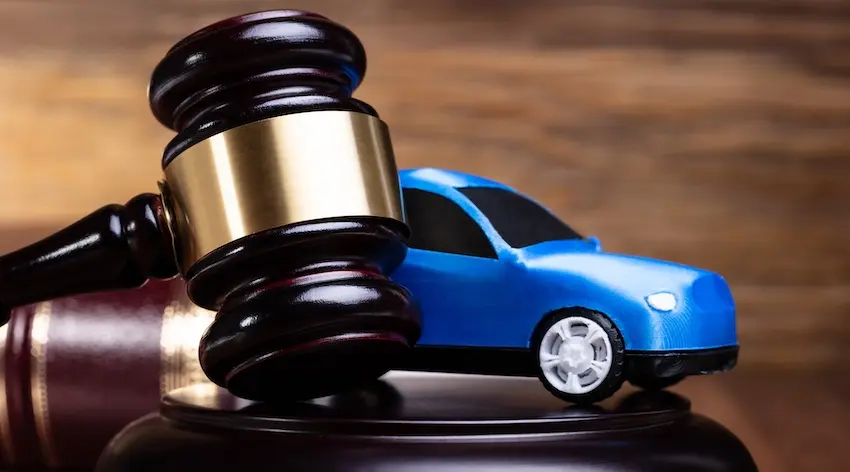 A dark wooden judge's gavel with a gold band rests against its sound block beside a small blue toy car on a warm wood grain surface representing the legal proceedings that accident victims may need to pursue after a car accident when insurance negotiations fail to produce fair compensation in Metro Atlanta.